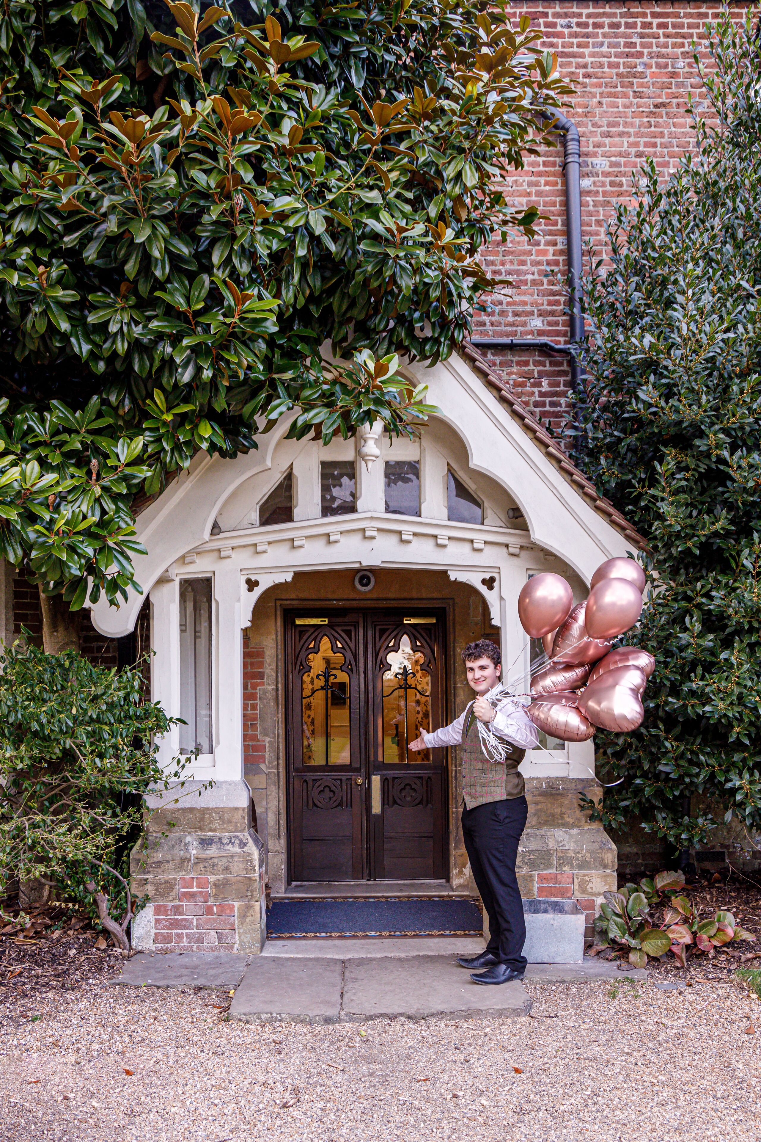 A person standing in front of a building with a brick facade and a decorative entrance.
