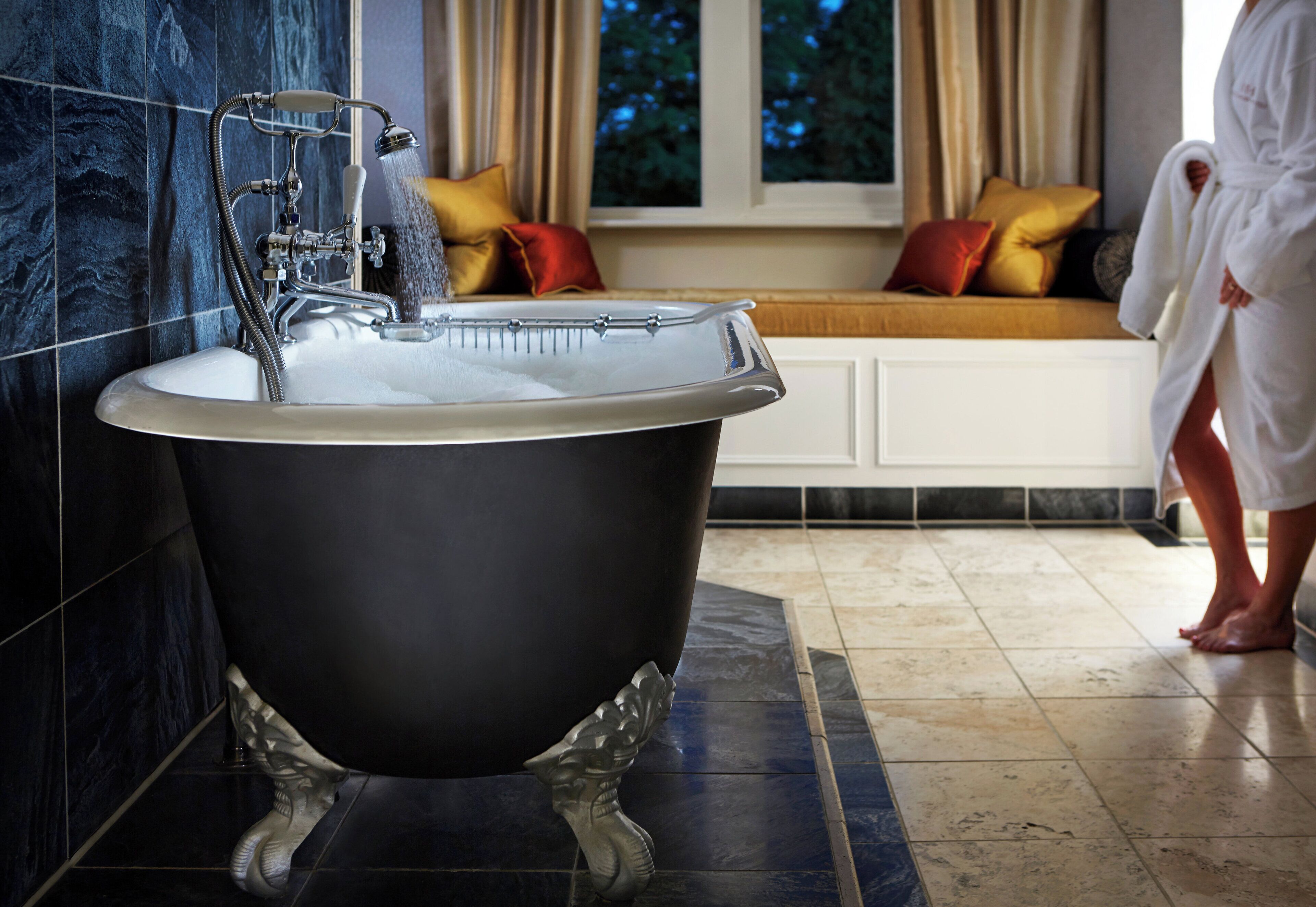 A clawfoot bathtub in a bathroom with a window seat and a view of trees outside.