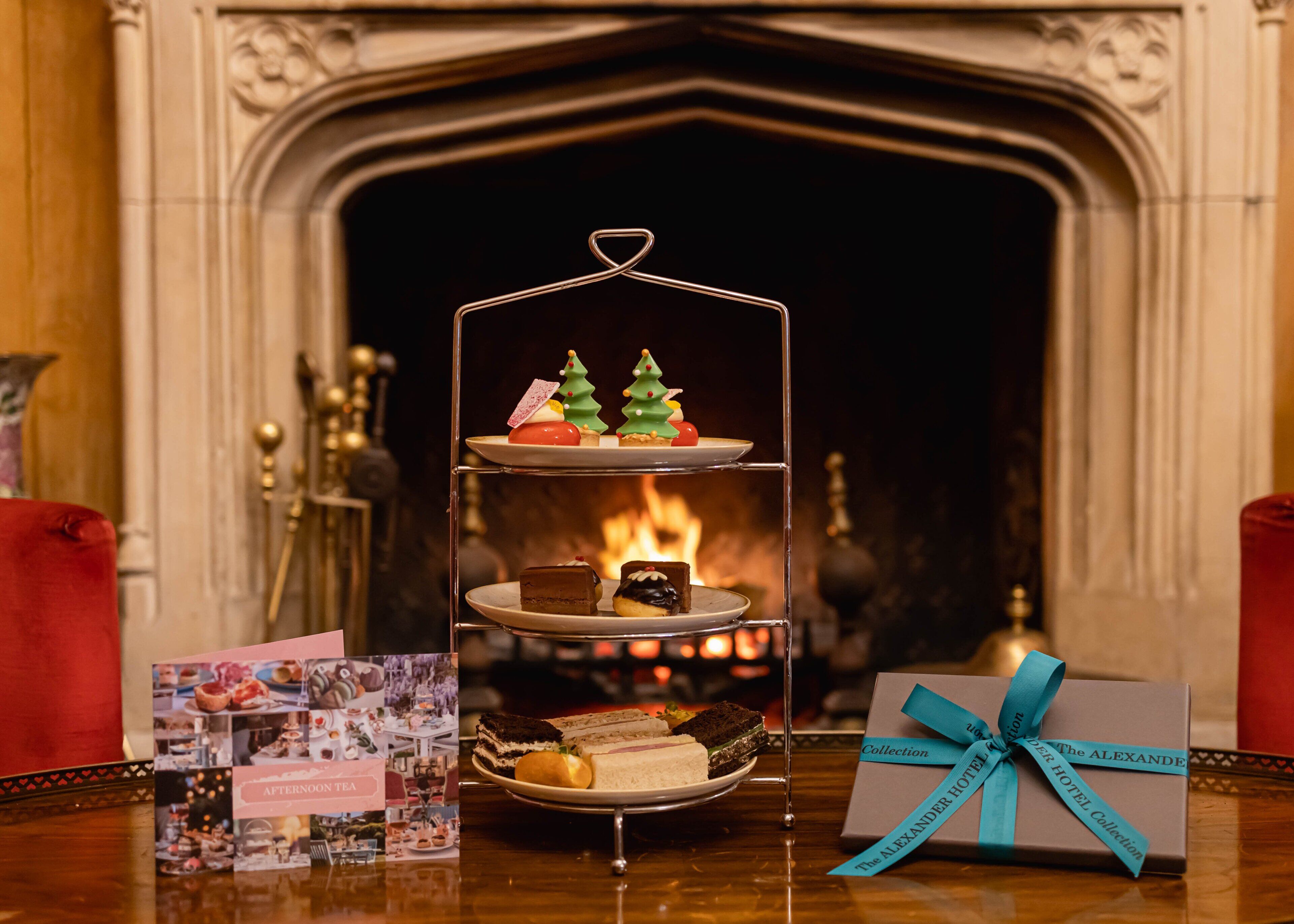 A three-tiered dessert stand with a Christmas tree decoration in front of a fireplace.