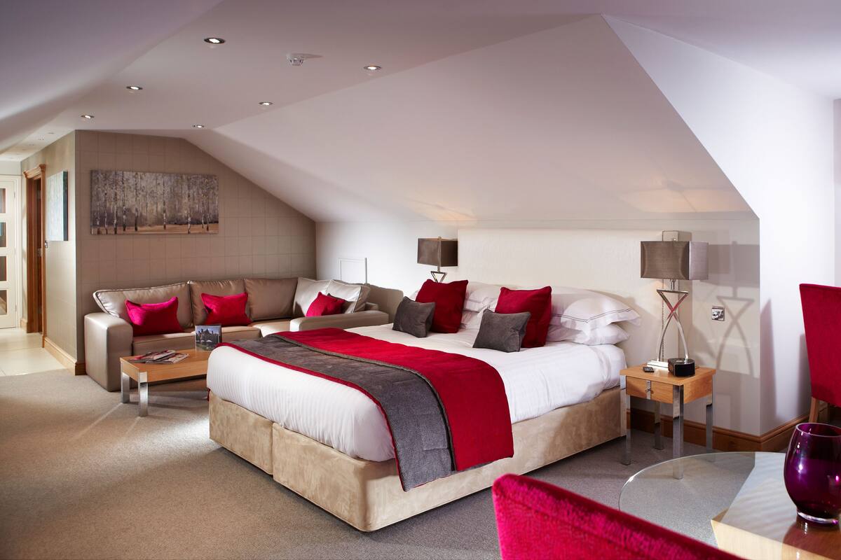 A modern hotel room with a large bed, a sofa, a desk, and a chair.