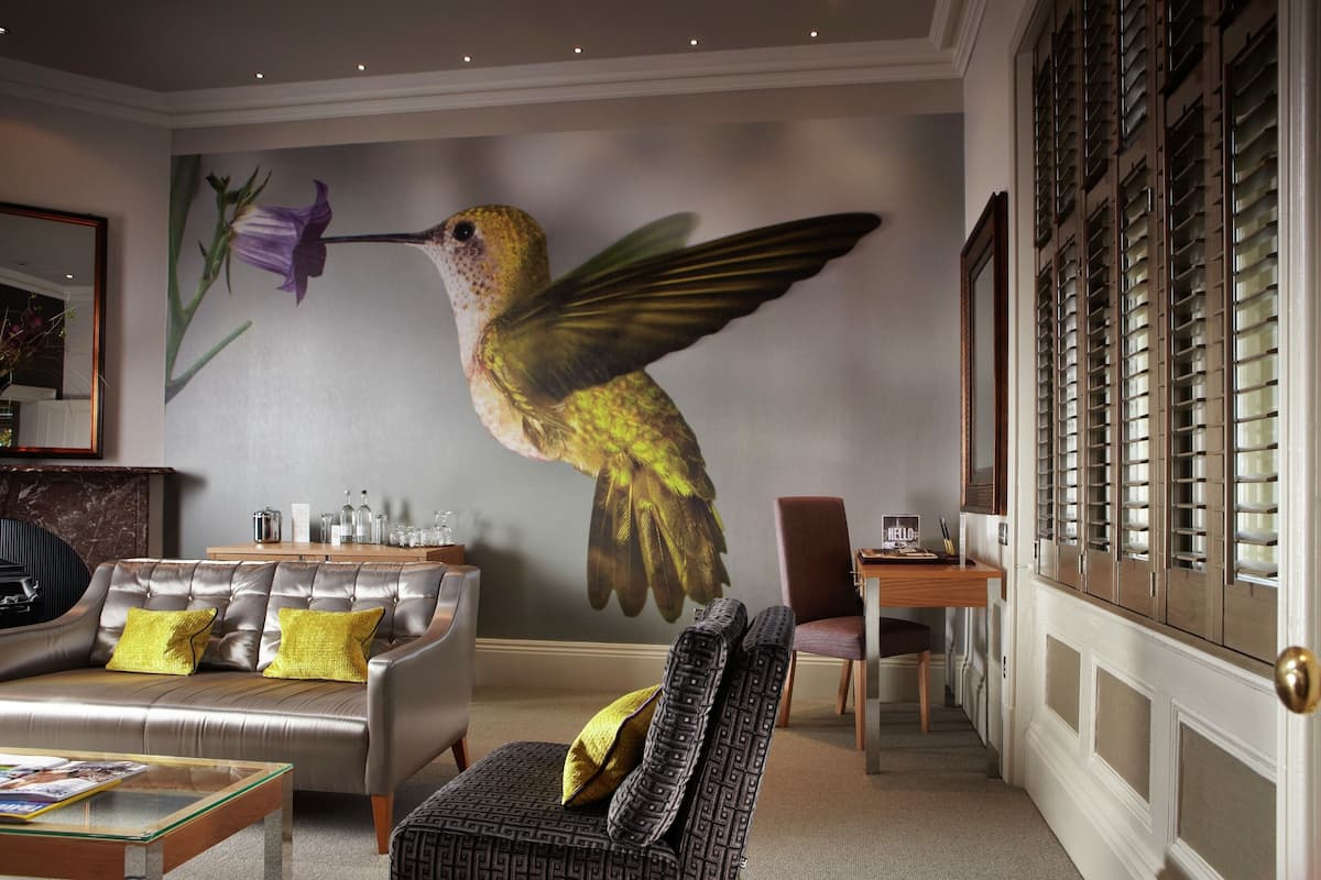 A living room with a large mural of a hummingbird, a leather sofa, a glass coffee table, and a patterned armchair.