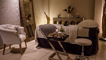A well-lit room with a bed, a chair, a vanity table, and a mirror.