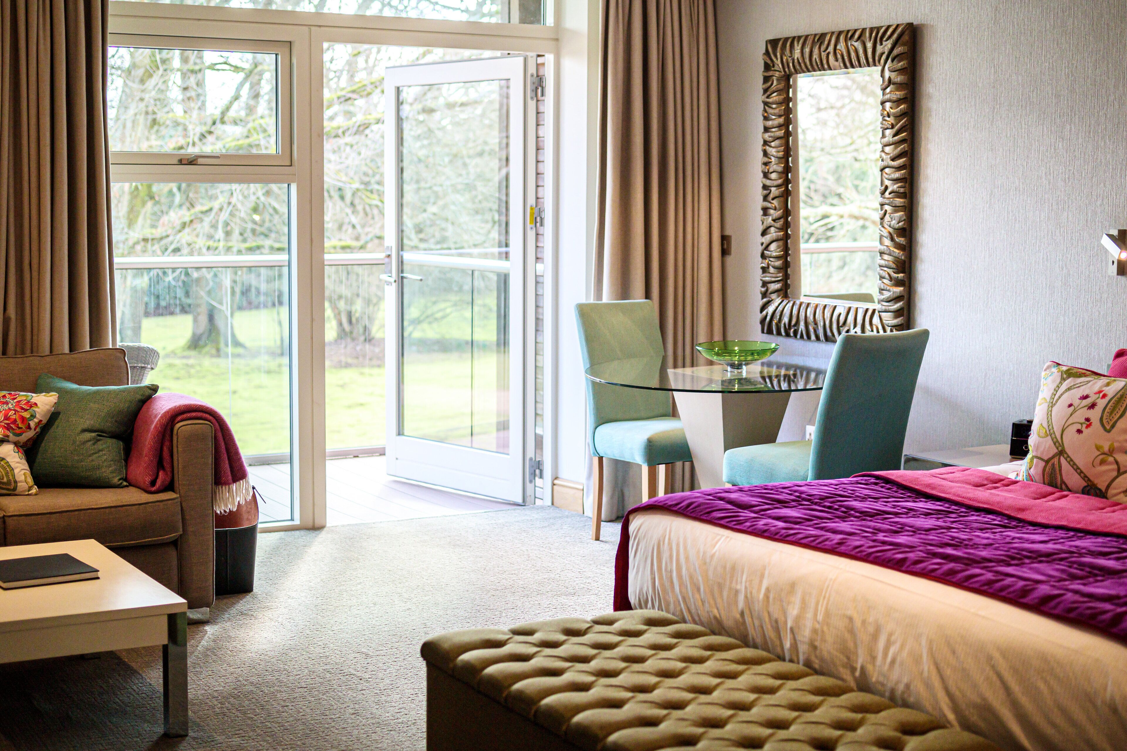 Une chambre d’hôtel avec un lit, un bureau, une chaise et un canapé. Une grande fenêtre offre une vue sur l’extérieur.
