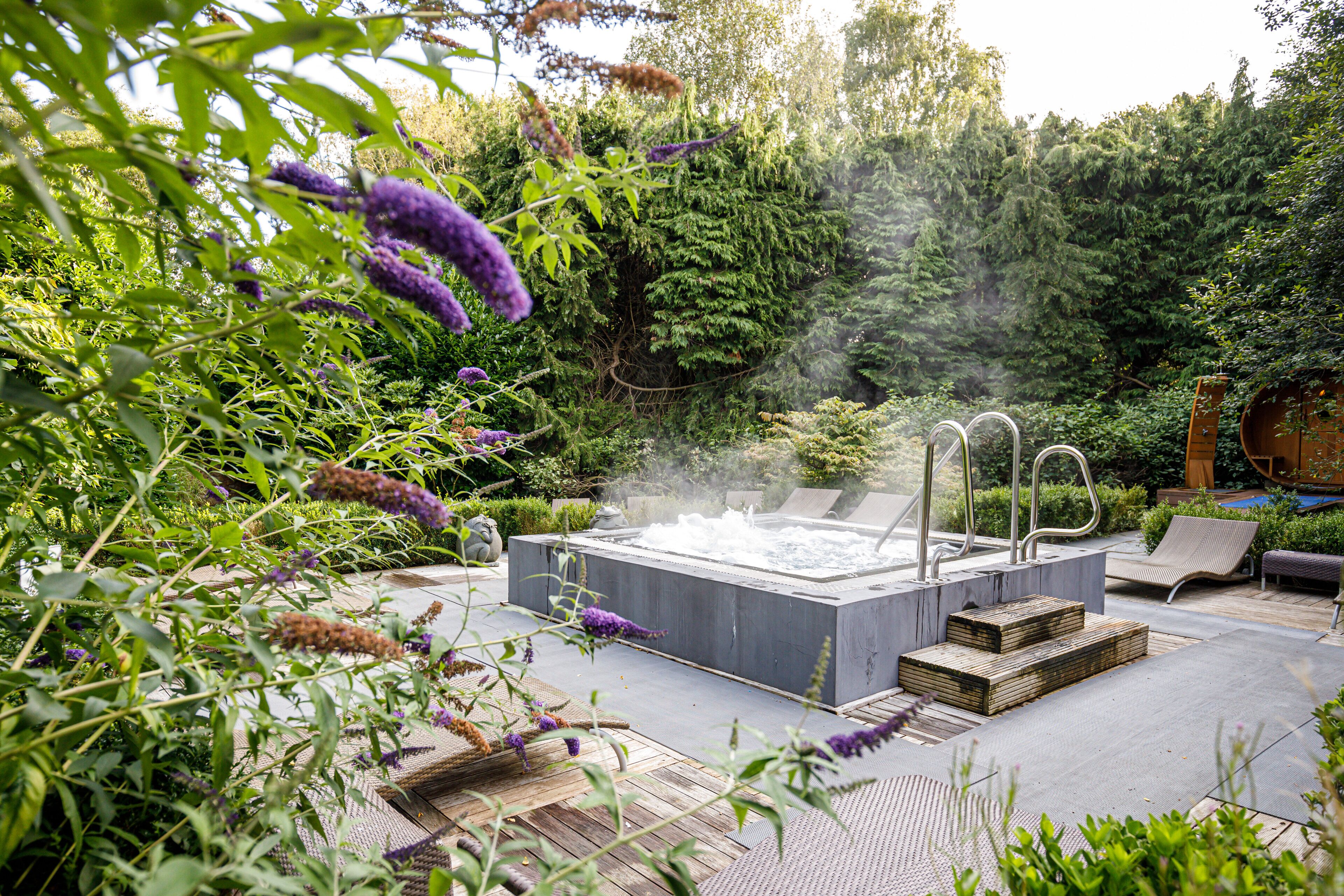 A hot tub surrounded by lush greenery and a wooden deck.