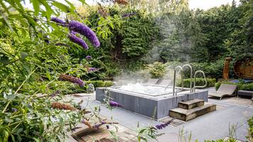 A hot tub surrounded by lush greenery and a wooden deck.