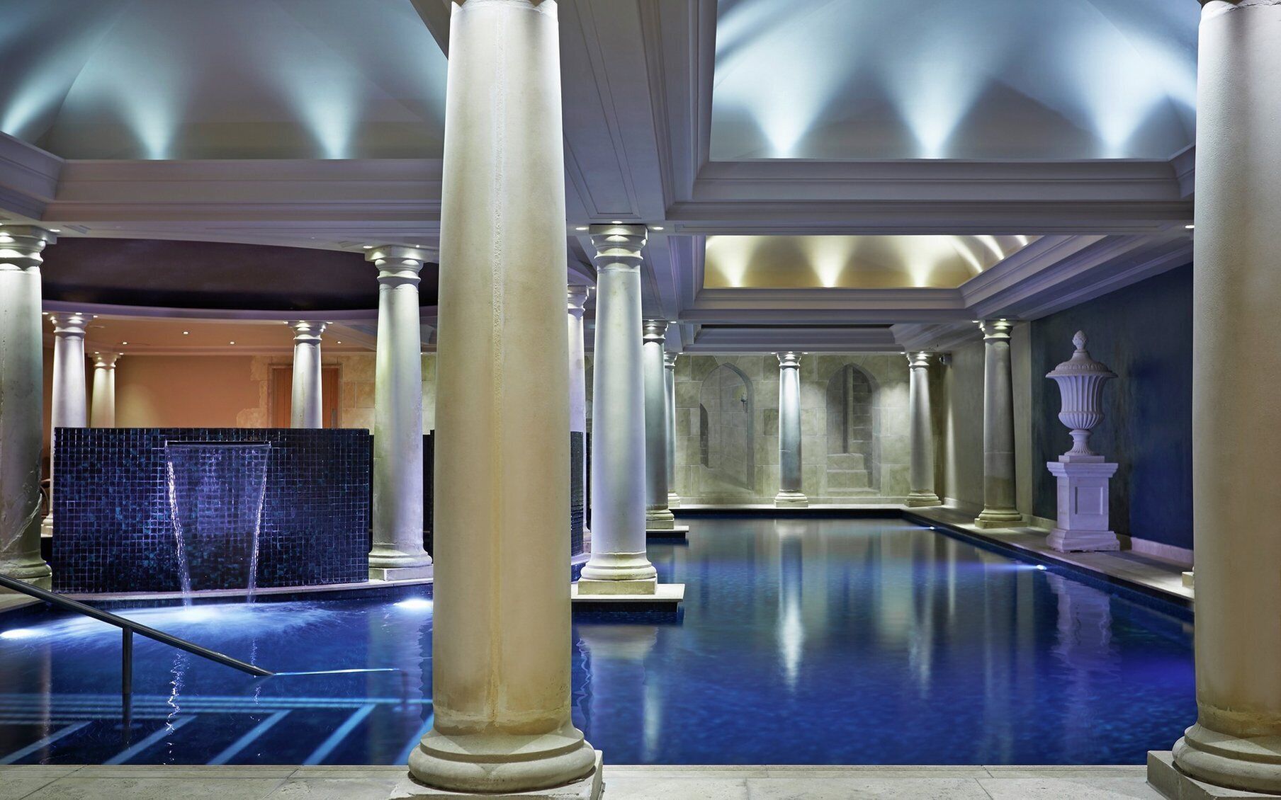 A spacious indoor swimming pool with columns and a tiled wall.