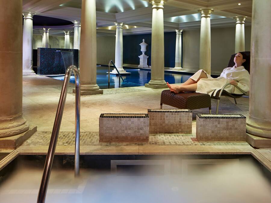 A spa area with a pool, columns, and a person relaxing on a chair.