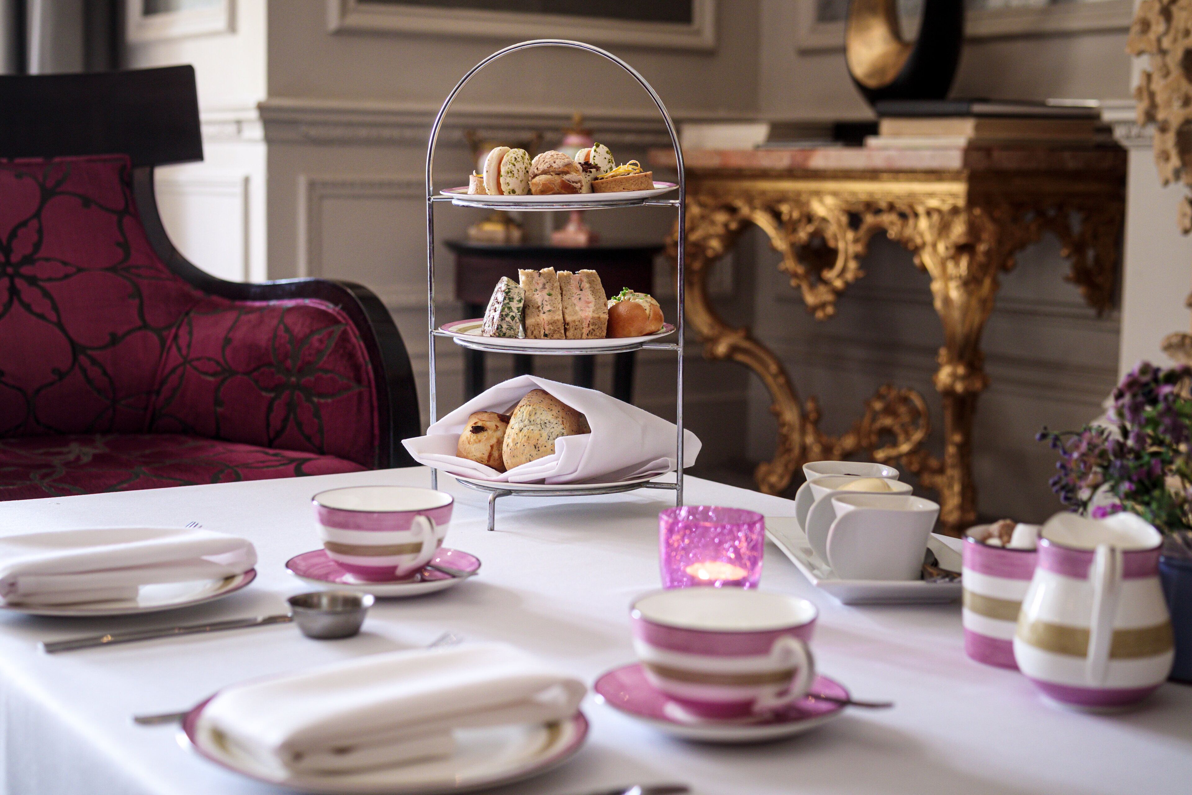 A three-tiered dessert stand with pastries, a table set with plates, cups, and a pink candle.