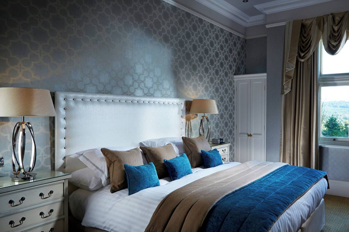 A neatly arranged bedroom with a large bed, bedside tables, and a view of the outdoors through a window.