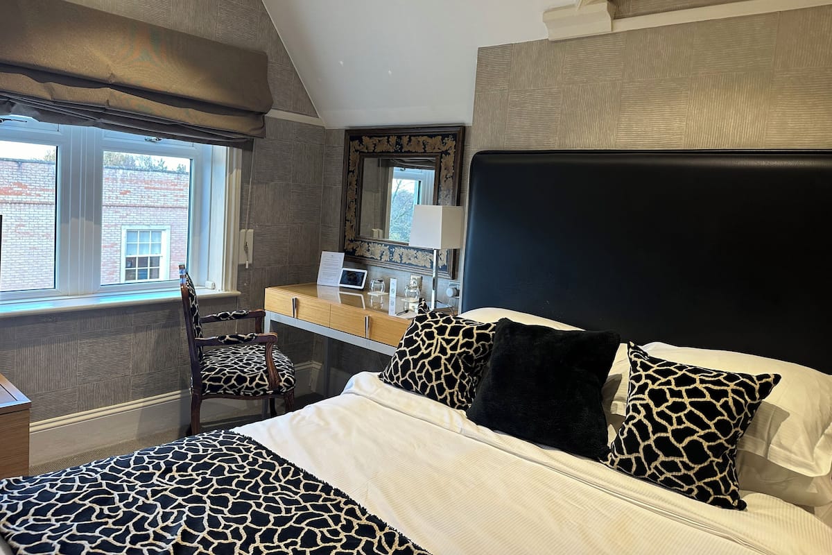 A bedroom with a bed, a desk, a chair, and a large window.