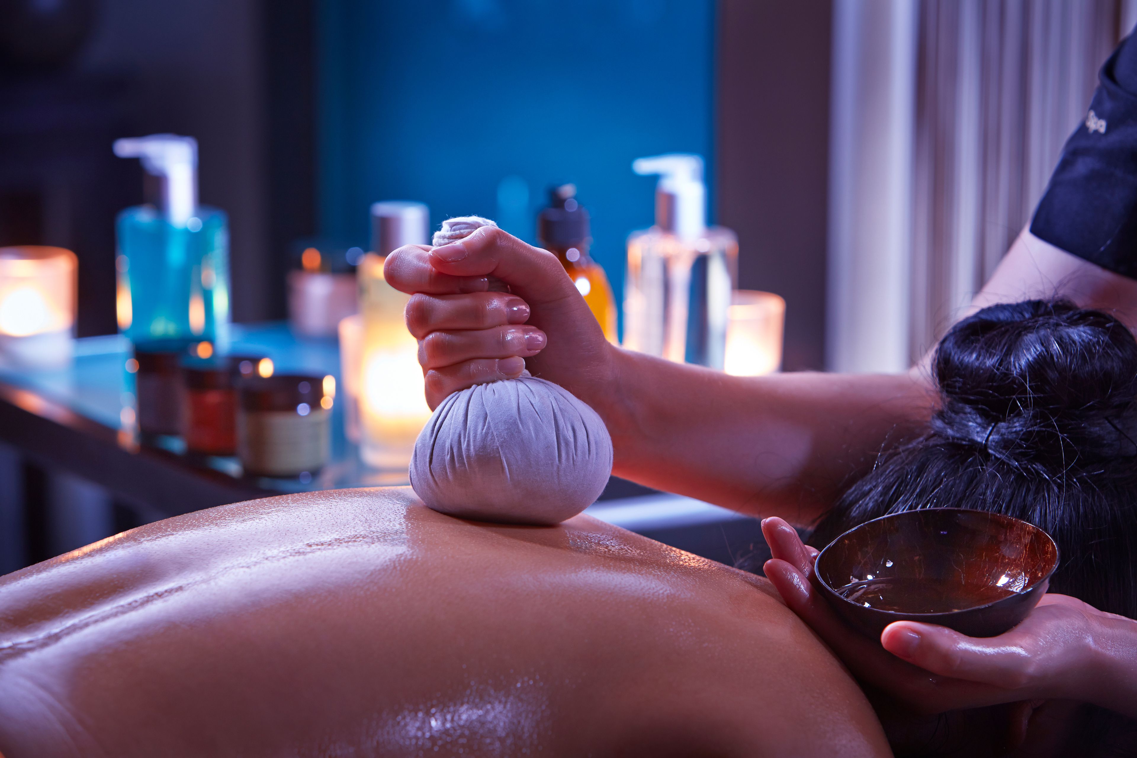 Eine Massageanwendung, wobei die Hände des Therapeuten und eine Öl-Schale im Fokus stehen.
