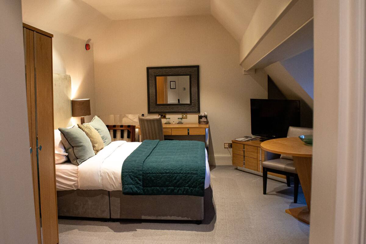 A bedroom with a bed, desk, chair, and TV.