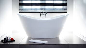 Ein modernes Badezimmer mit freistehender Badewanne, einem Fenster mit horizontalen Jalousien und einer Ablage mit Toilettenartikeln.