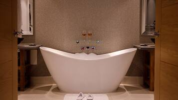 A modern bathroom with a freestanding bathtub, a glass shelf with toiletries, and a towel on the floor.