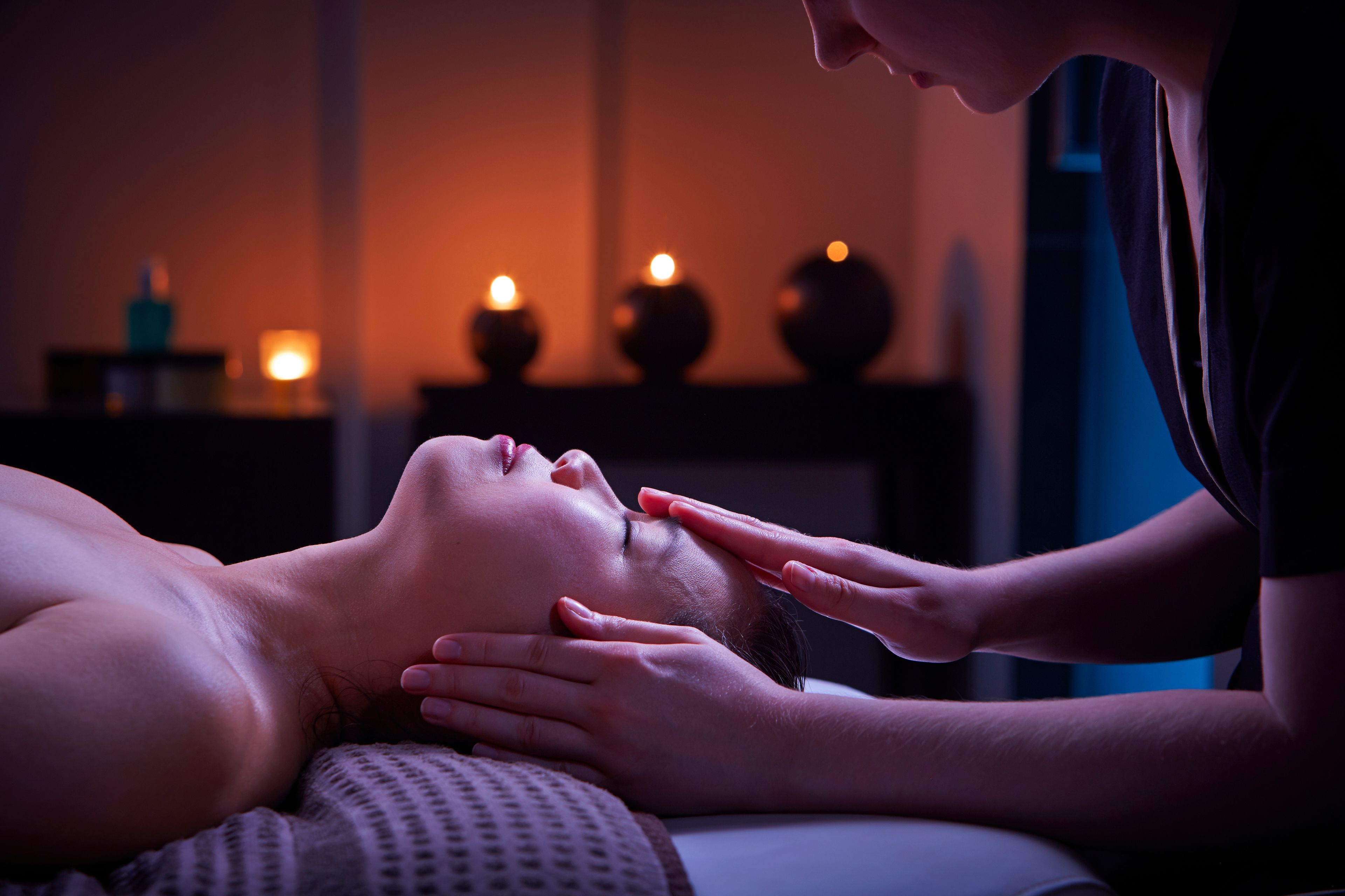A person receiving a massage in a dimly lit room with candles on a table.