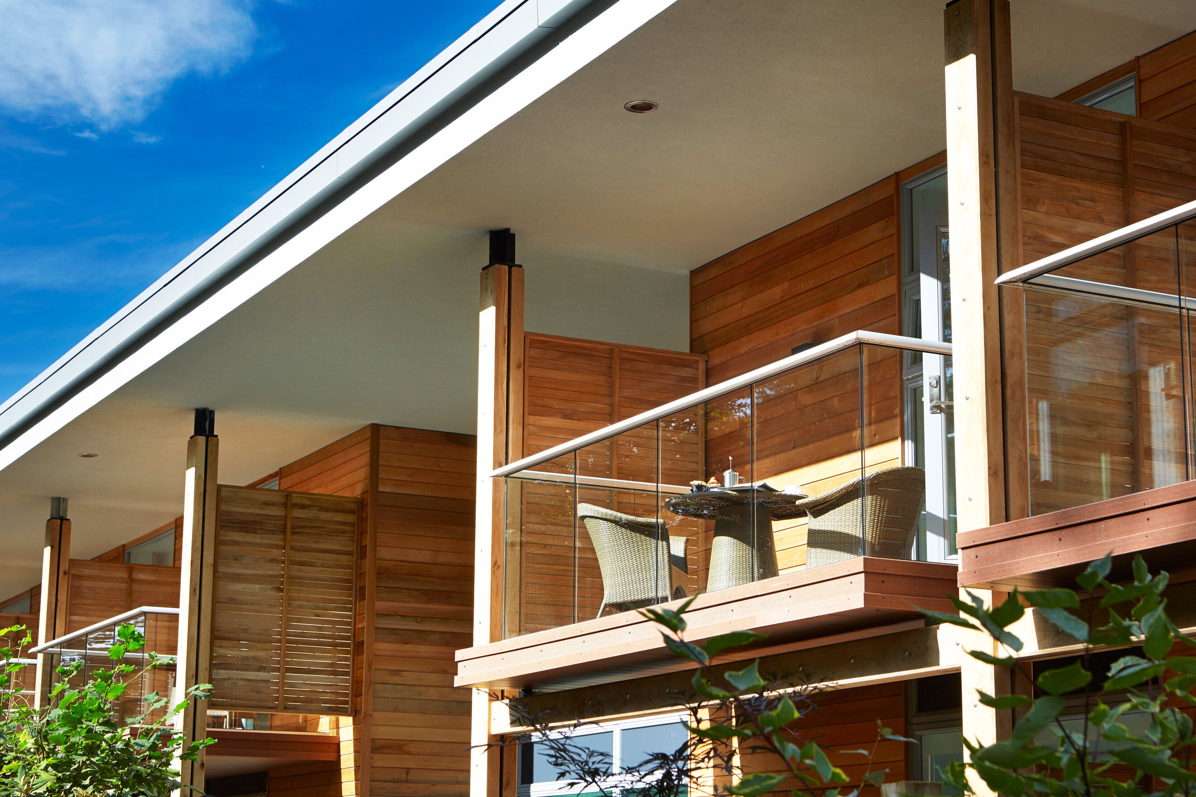 A modern building with wooden paneling, large windows, and a balcony with wicker furniture.