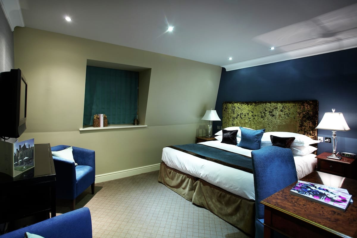 A hotel room with a bed, a desk with a computer, a chair, a window, and a television.
