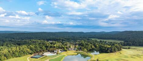 A golf course with a lake, surrounded by forested hills and a clear sky.