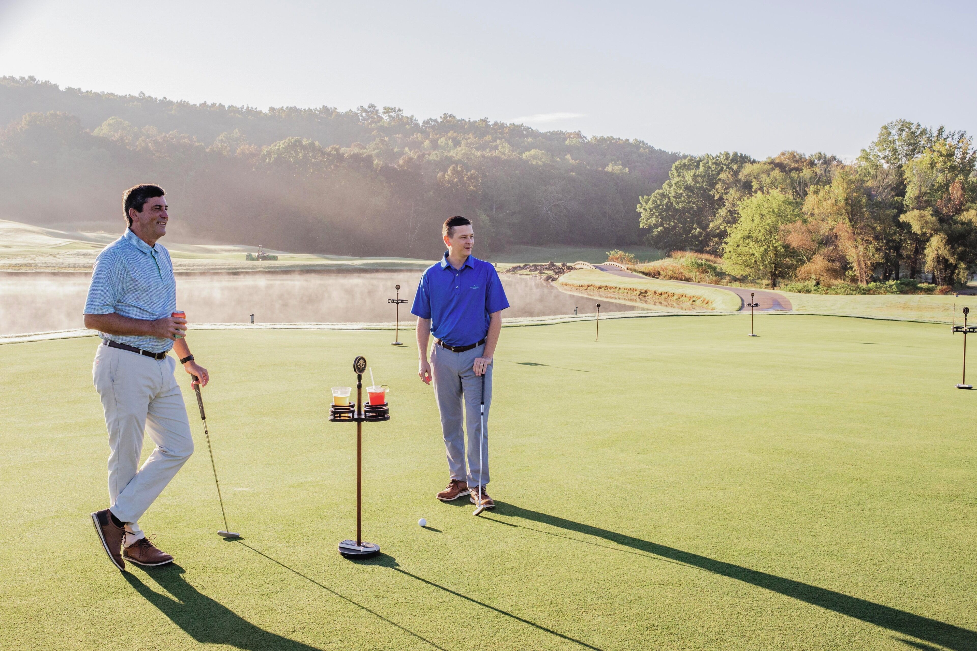 Two people on a golf course with a putting green and a flagstick.