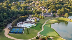 Luchtbeeld van een golfbaan met een zwembad, tennisterreinen en een groot huis omringd door bomen.
