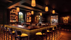 Een bar met een lange toonbank, meerdere hanglampen en barstoelen.