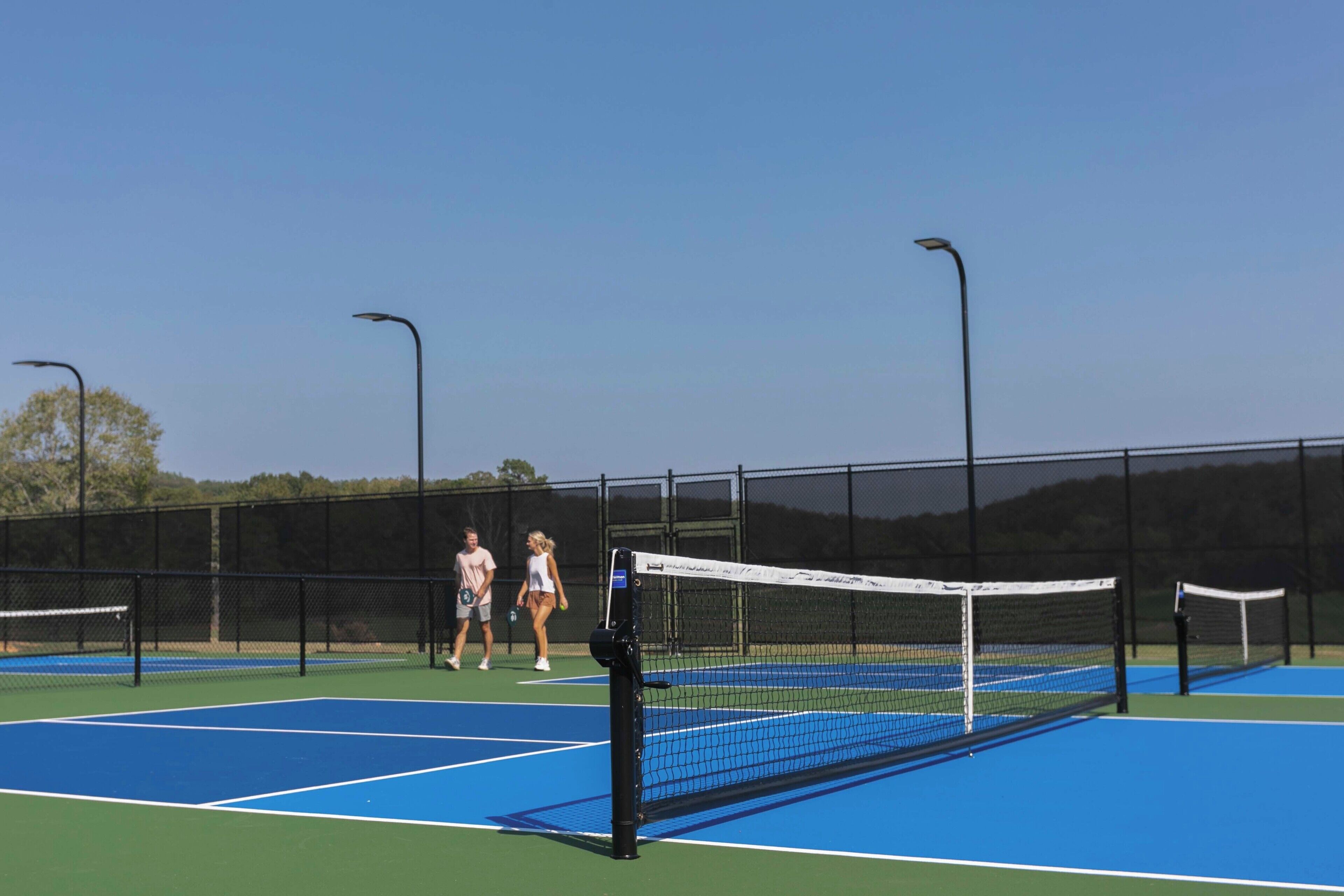 A tennis court with a net, two players, and a fence.