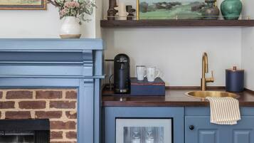 A kitchen with a blue cabinet, a coffee maker, two mugs, a sink, and a vase with flowers on the counter.