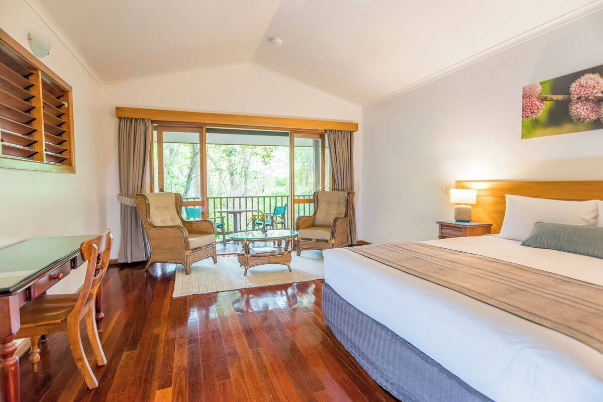 A hotel room with a bed, a desk, and a balcony with chairs.
