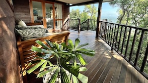 A wooden deck with a sofa and a potted plant, a glass door leading to an interior space, and a view of the ocean. - Thala Beach Nature Reserve (Oak Beach)