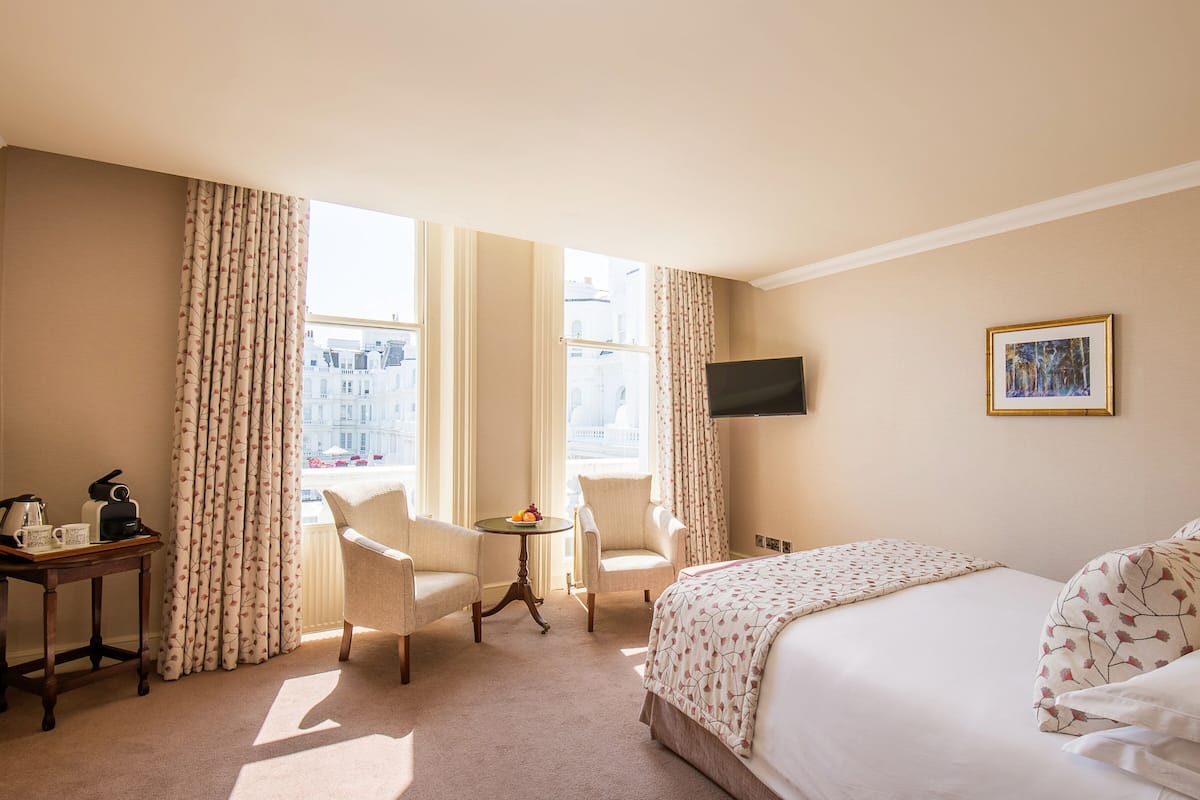 Habitación de hotel con cama, dos sillones, una mesita con frutero, cafetera y televisor en la pared.