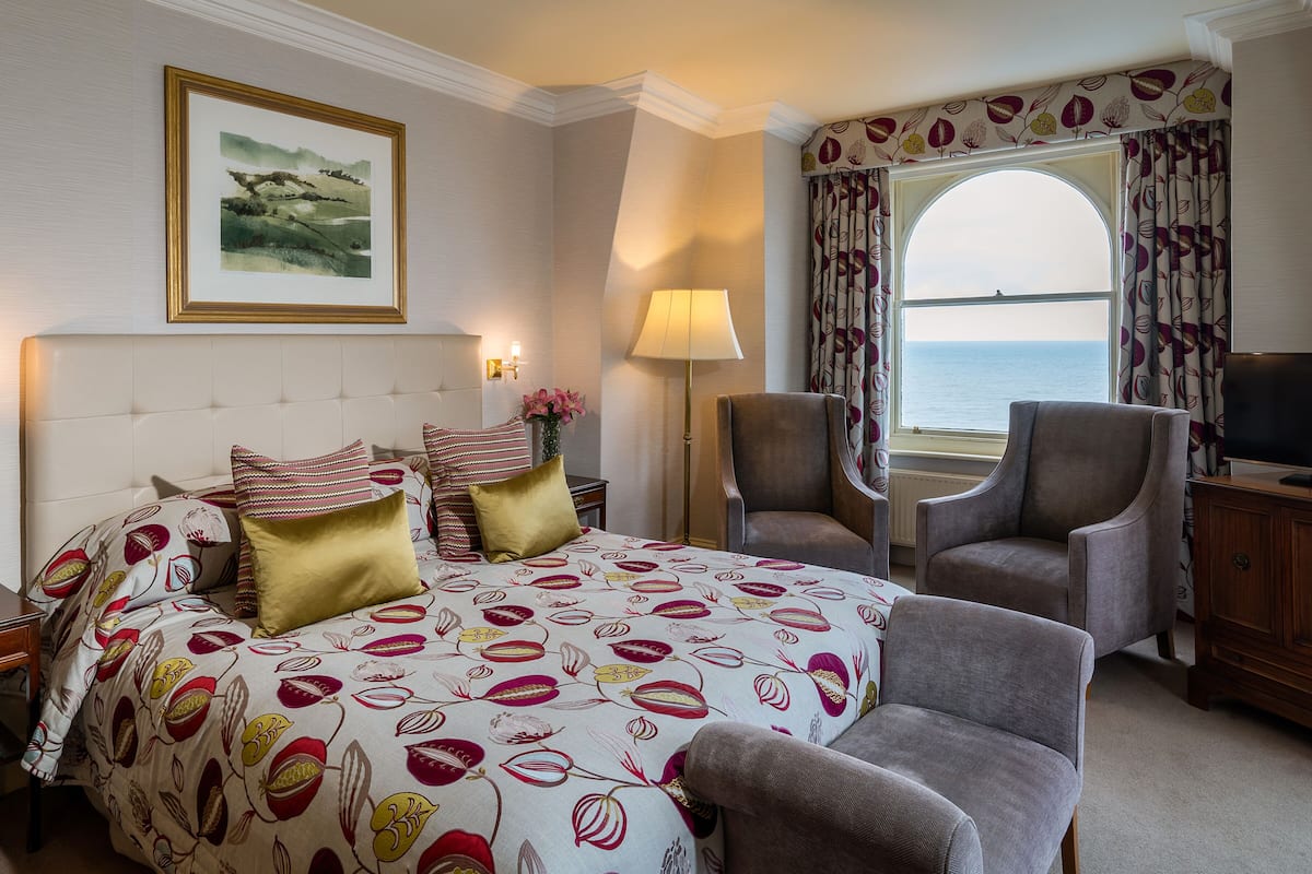 Una habitación de hotel con una cama, dos sillones, un escritorio, una lámpara y un televisor.
