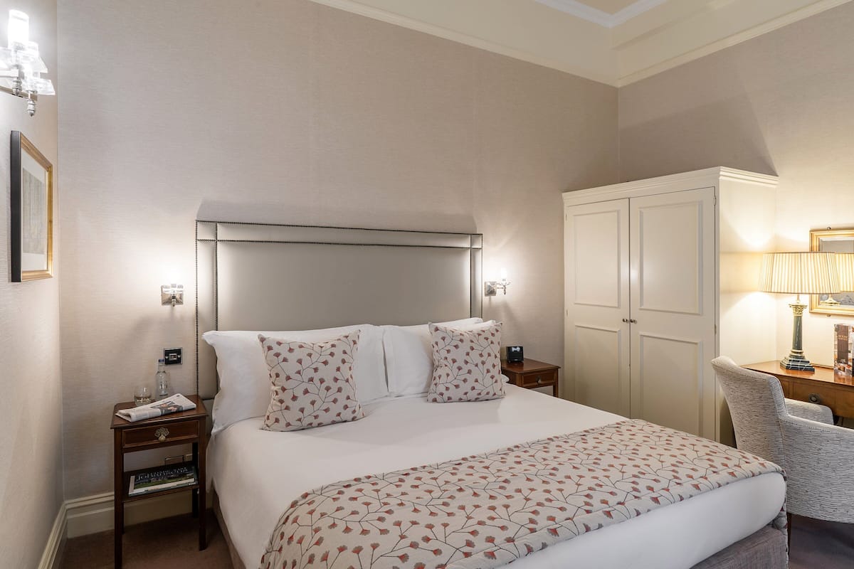 Habitación de hotel con una cama grande, una mesita de noche con lámpara, una silla y un armario.