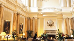 Un vaste hall d’entrée avec de hauts plafonds, des colonnes richement décorées, un lustre et une cheminée.