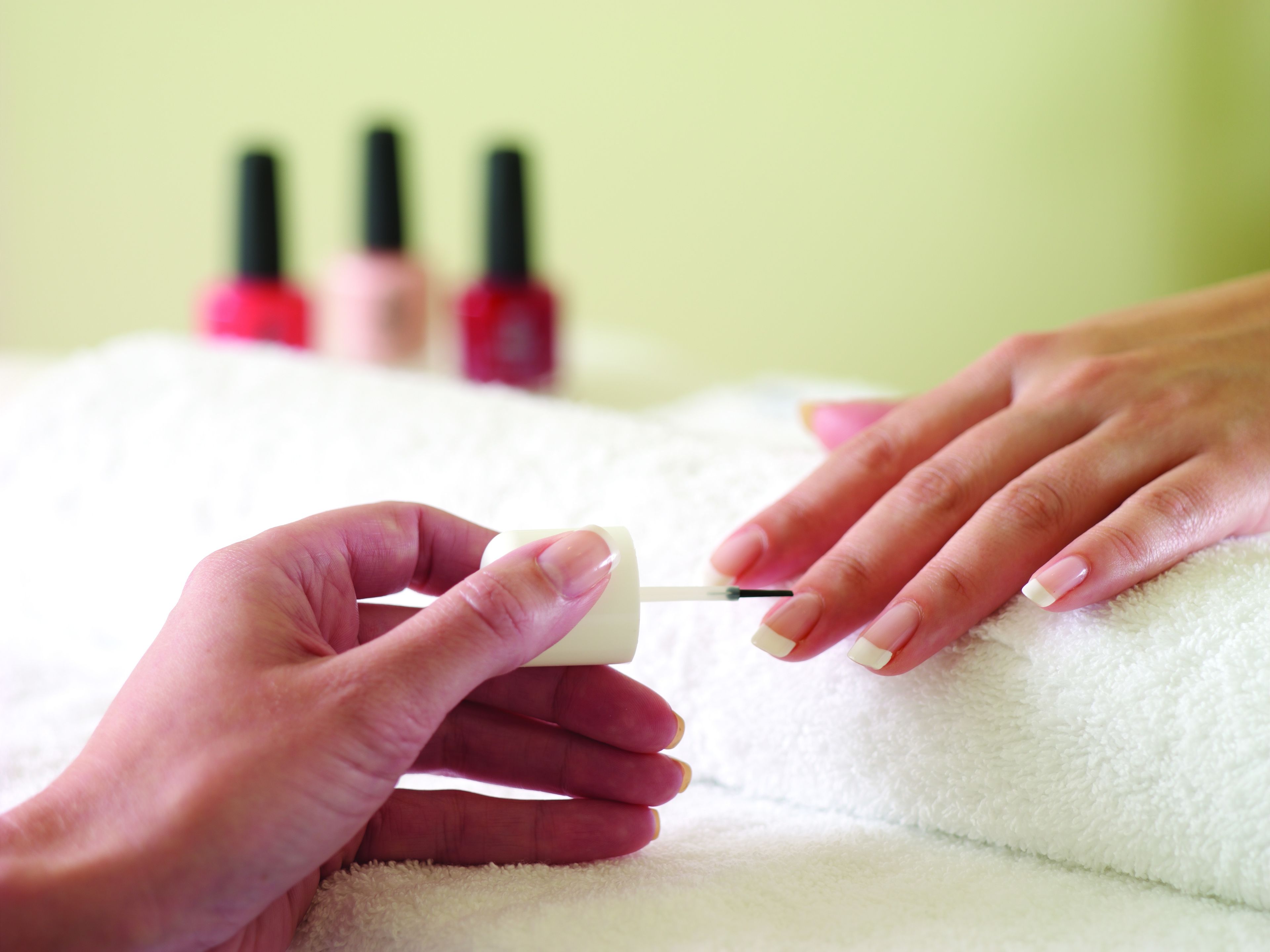 A close-up of a person painting a nail with a nail polish brush.