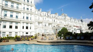 Une grande piscine où une personne nage, entourée d’un bâtiment blanc doté de nombreuses fenêtres et de balcons.