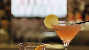 Zwei Cocktails auf einer Bartheke, einer im Kurzglas und einer im Martini-Glas, mit unscharfem Hintergrund, der eine Bar andeutet.