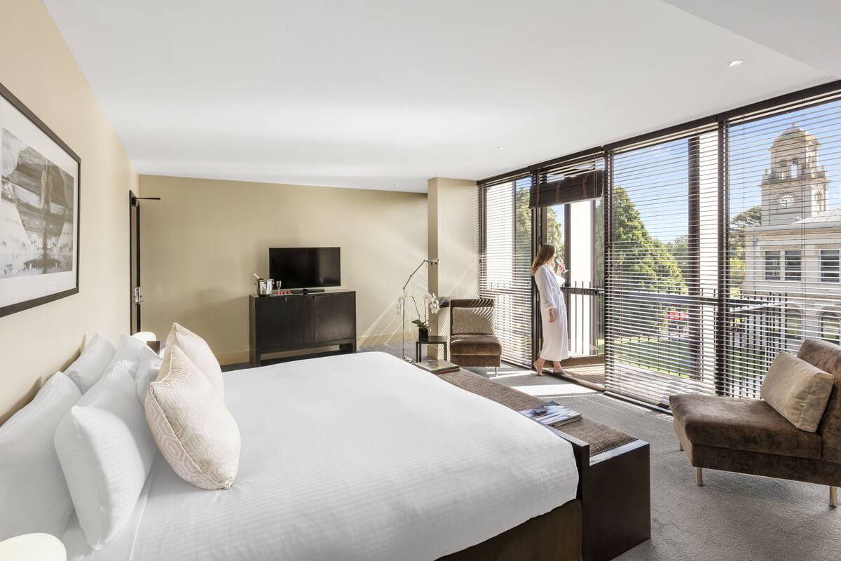 Una habitación de hotel moderna con una cama grande, televisión, escritorio y balcón con vistas a un edificio.