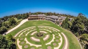 An aerial view of a large estate with a circular lawn design, a prominent building with multiple windows, and surrounding greenery. - Lancemore Mansion Hotel Werribee Park (Werribee South)