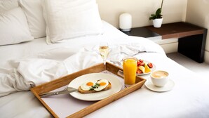 A neatly made bed with white linens, a tray with breakfast including toast, eggs, coffee, and juice, and a bedside table with a plant and a candle. - Lancemore Mansion Hotel Werribee Park (Werribee South)