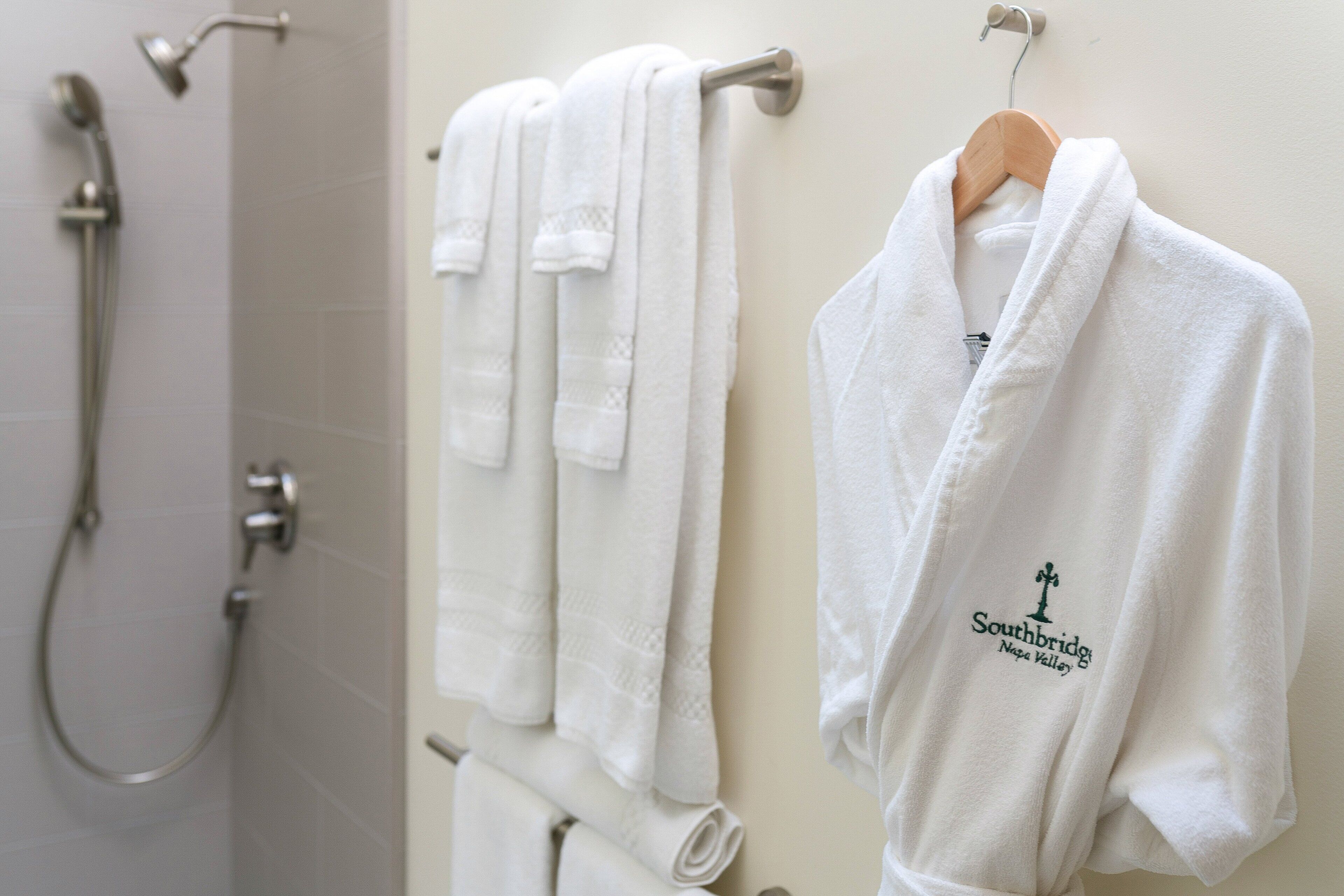 A bathroom with white towels, a shower, and a robe with a logo.
