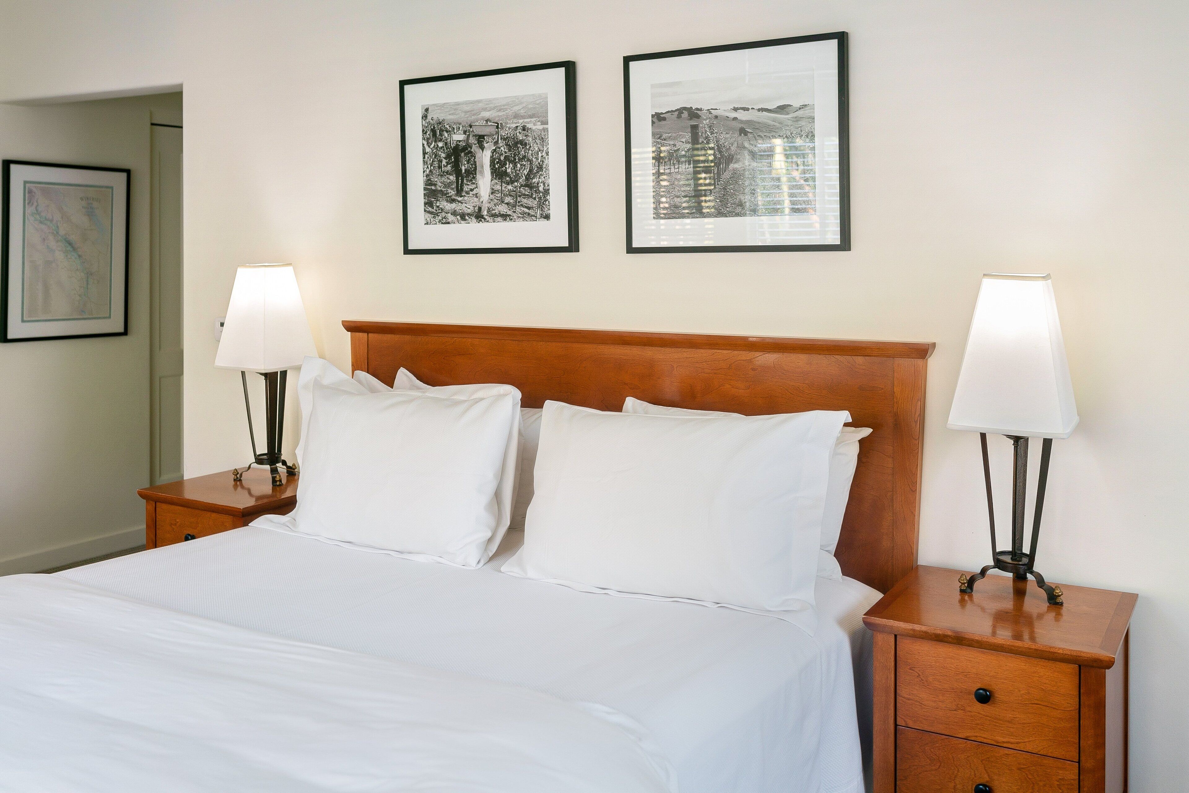 A neatly made bed with white linens, two bedside tables with lamps, and two framed black and white photographs on the wall.