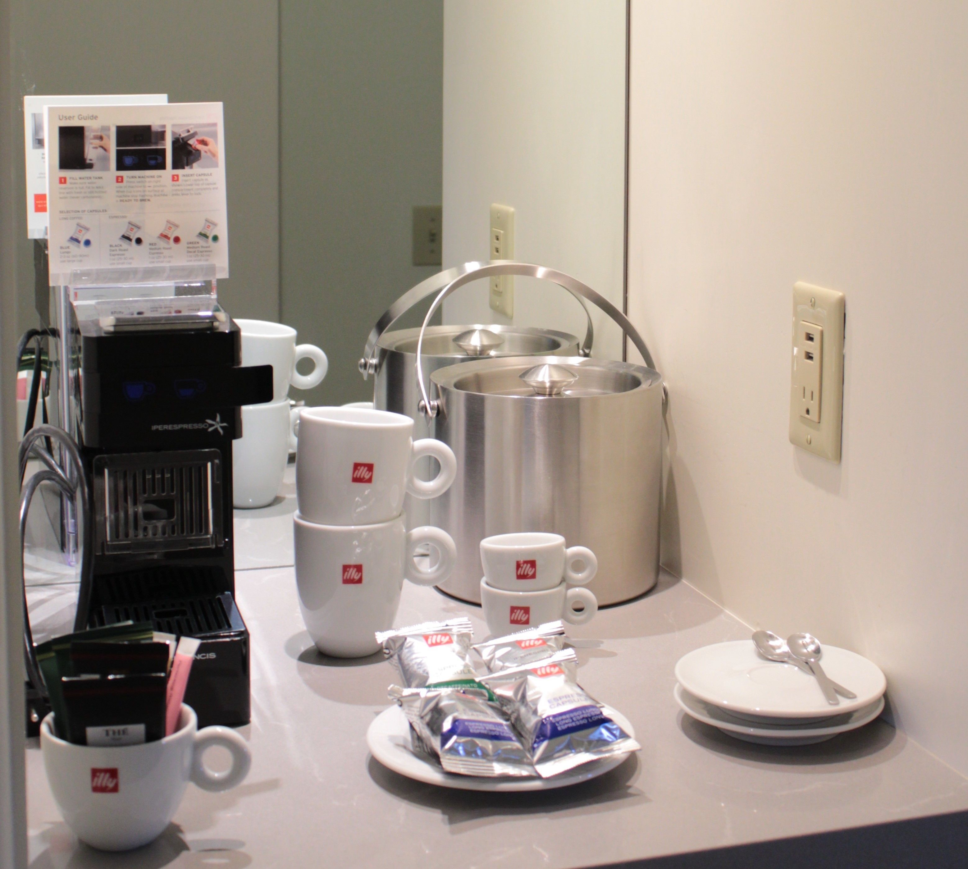 A coffee station with an espresso machine, multiple coffee cups, a kettle, and tea packets.