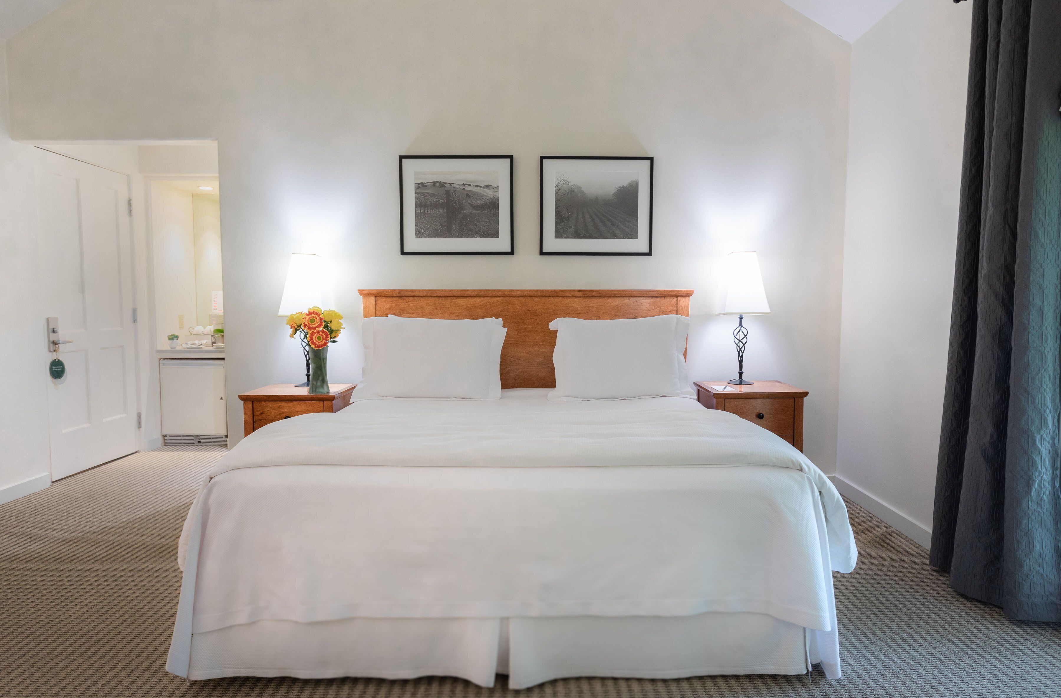 A hotel room with a large bed, two bedside lamps, a wooden headboard, and two framed pictures on the wall.