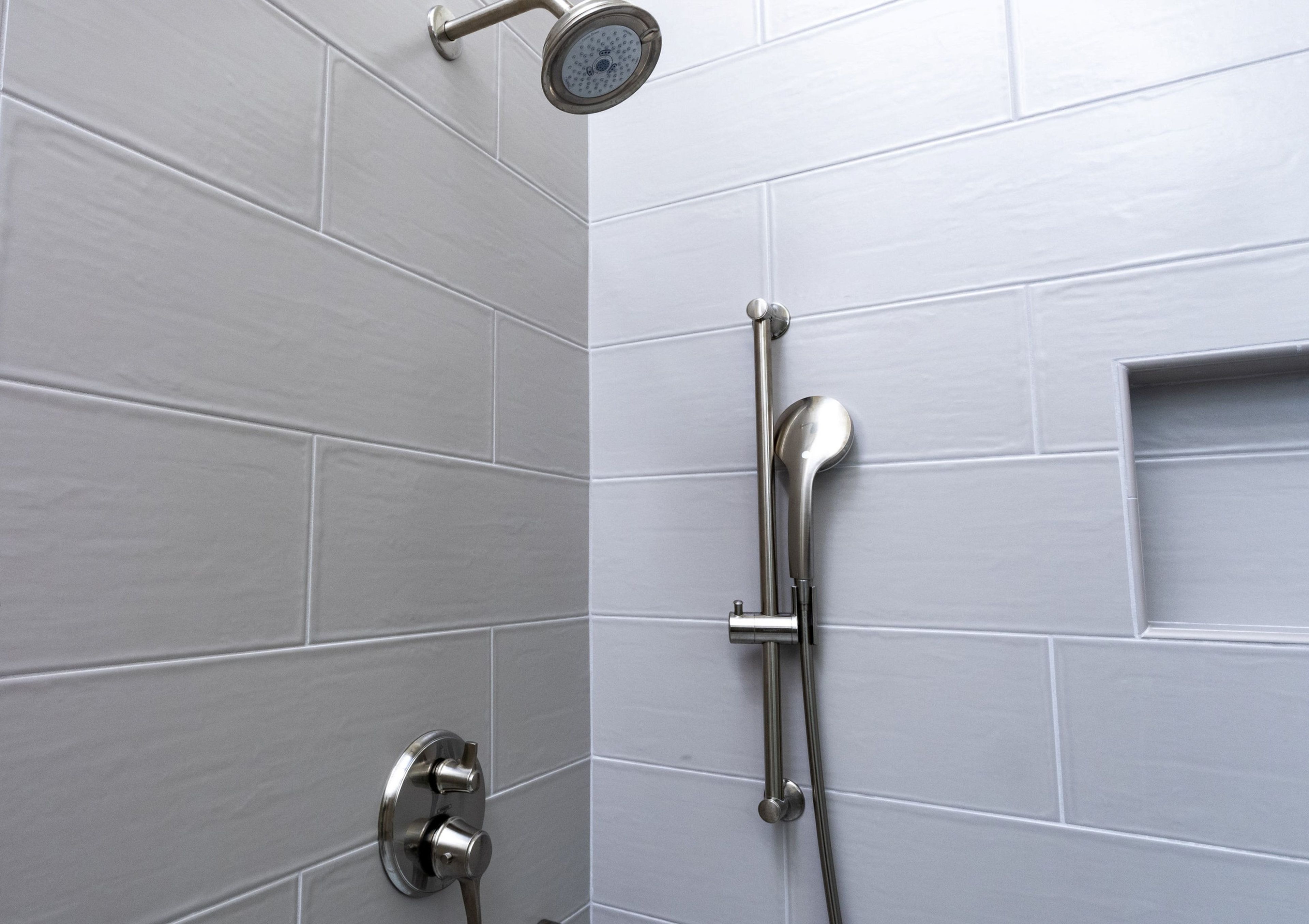 Ducha con cabezal de ducha de mano y panel de control en la pared.