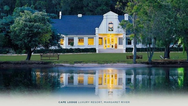 A waterfront property with a reflective pool, a white building with a blue roof, and a bench in the foreground. - Cape Lodge (Wilyabrup)