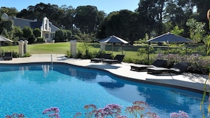 A swimming pool with lounge chairs and umbrellas, surrounded by a fence and greenery. - Cape Lodge (Wilyabrup)