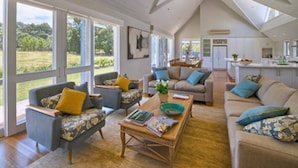 A spacious living room with a high ceiling and large windows, a kitchen with white cabinets, and a dining area with a table and chairs. - Cape Lodge (Wilyabrup)