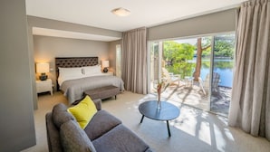 A bedroom with a bed, bedside tables, a sofa, a small table, and a view of a lake through large windows. - Cape Lodge (Wilyabrup)