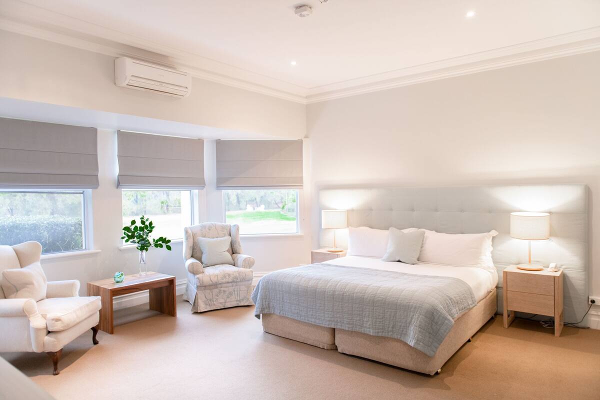A spacious bedroom with a large bed, two bedside tables, a chair, and a small table with a plant.