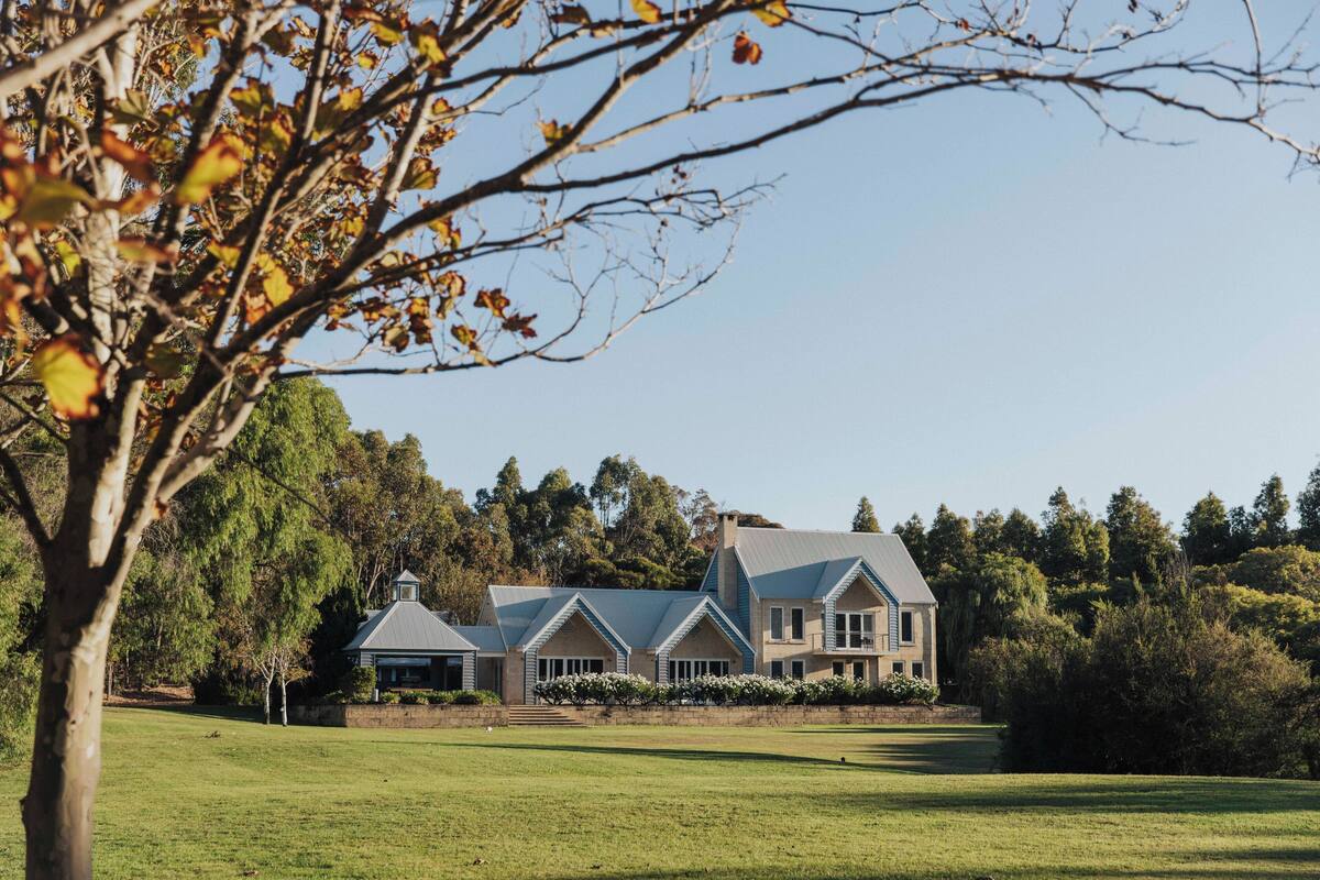 A large, two-story house with a prominent chimney, surrounded by a well-maintained lawn and trees.